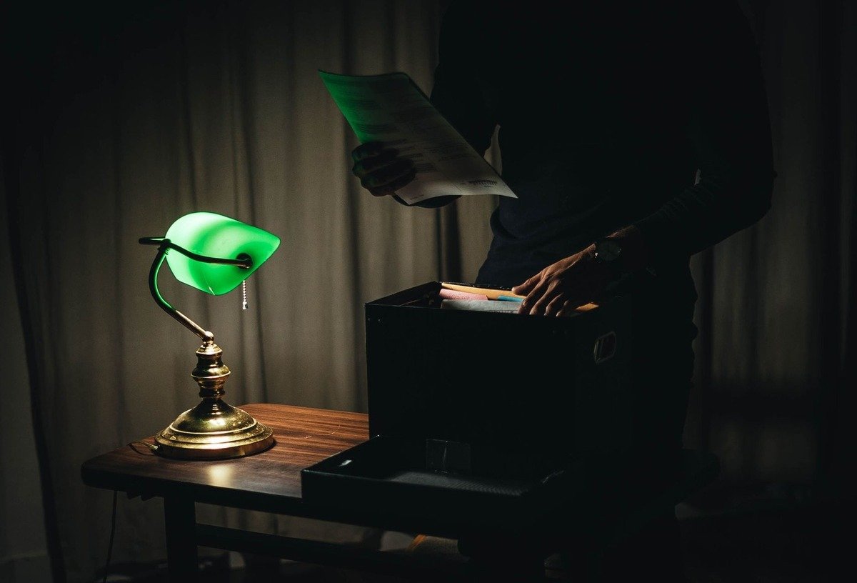 Une personne lit un document sous une lampe verte sur une table en bois
