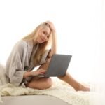 Femme travaillant sur son ordinateur portable, assise confortablement sur un lit dans un cadre lumineux