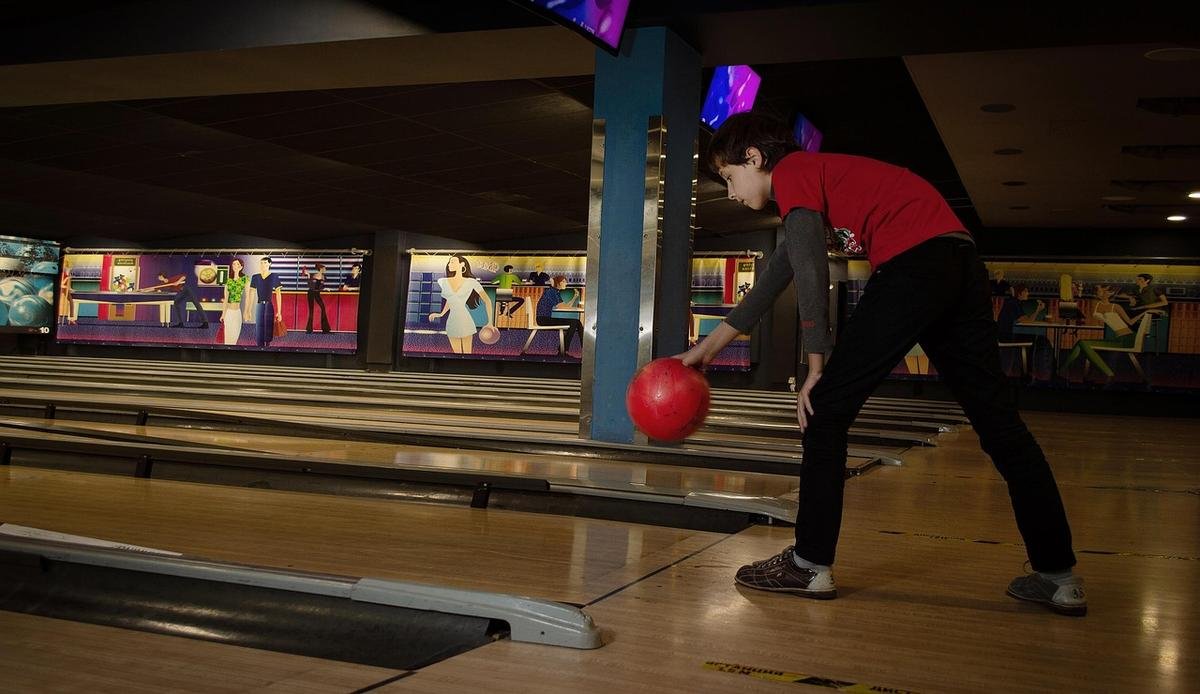 Un joueur lance une boule rouge sur une voie de bowling