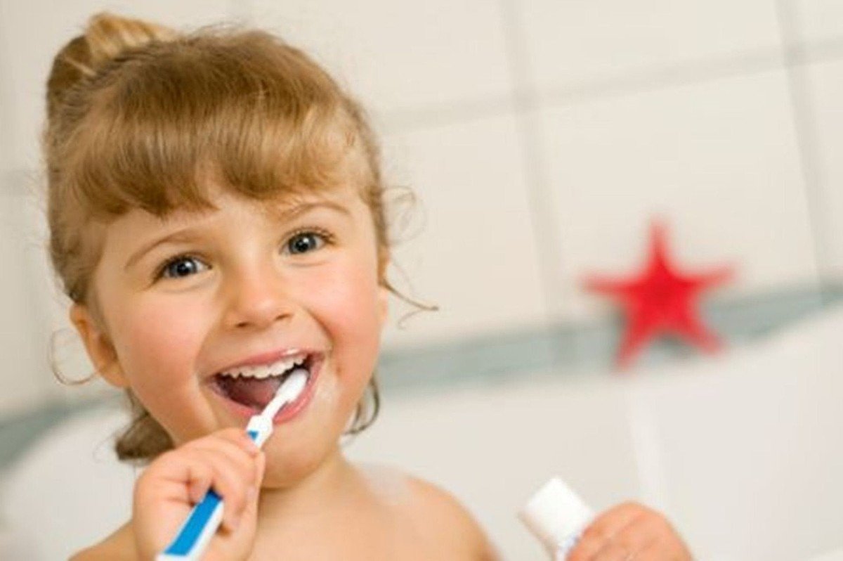 Jeune enfant souriante brossant ses dents avec une brosse à dents bleue