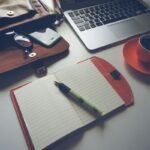 Un ordinateur portable, une tasse de café sur une soucoupe, un agenda ouvert avec un stylo, et un portefeuille sur une table