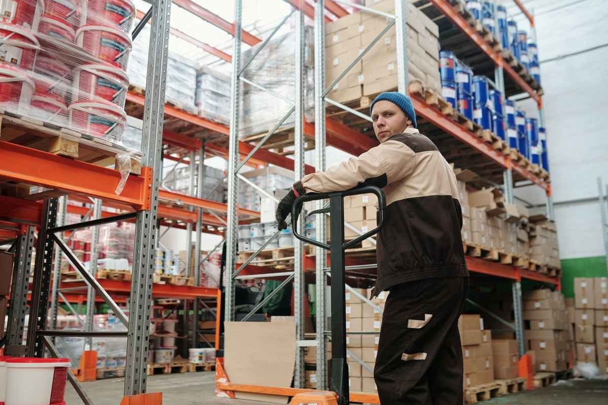 Employé sur chariot élévateur dans un entrepôt rempli de palettes et de produits