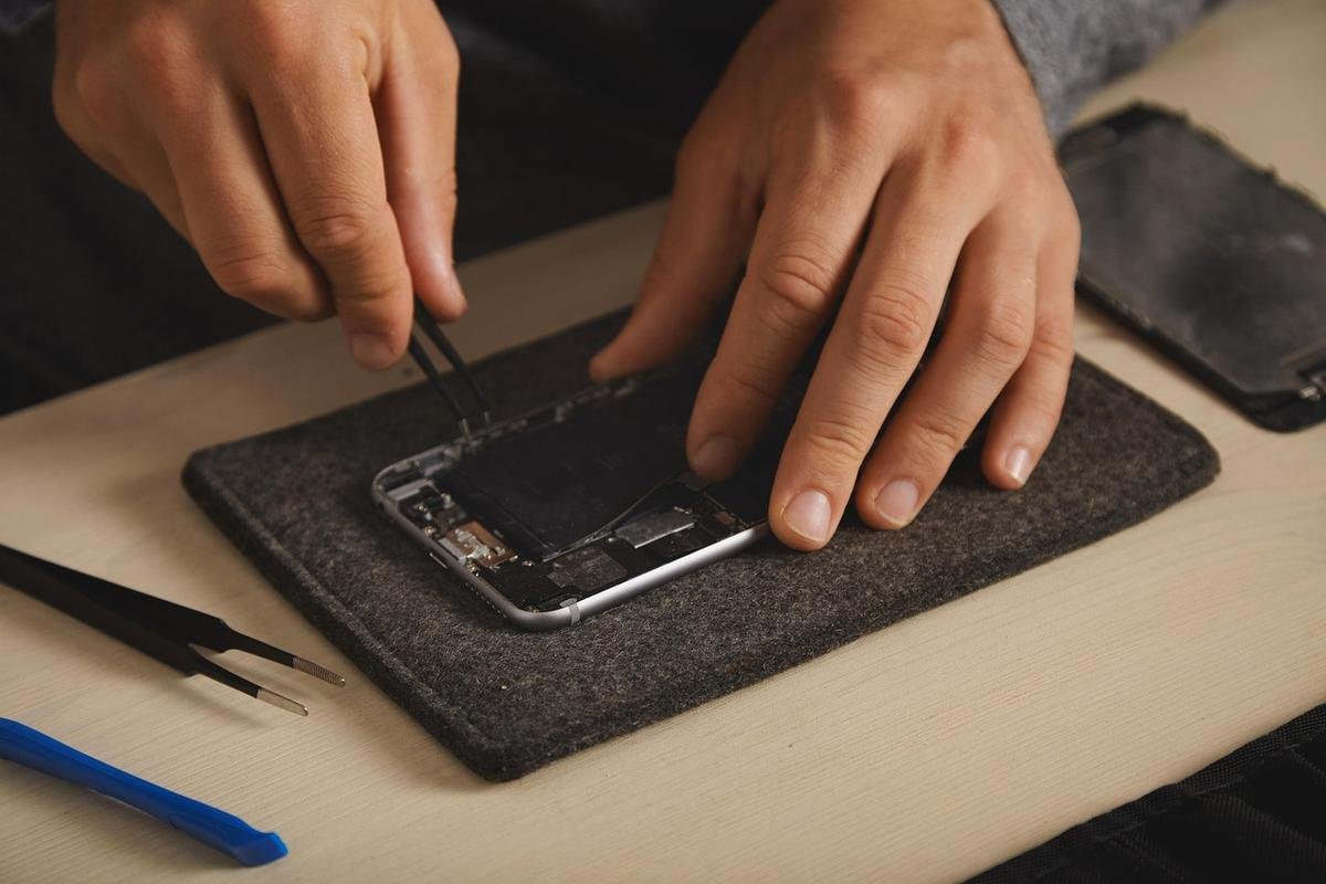 mains manipulant des pinces pour réparer un smartphone sur un tapis