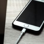 Un téléphone iPhone blanc connecté à un câble de recharge sur une surface grise