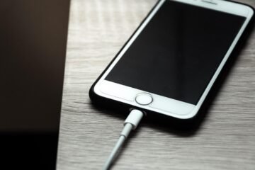 Un téléphone iPhone blanc connecté à un câble de recharge sur une surface grise