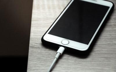 Un téléphone iPhone blanc connecté à un câble de recharge sur une surface grise