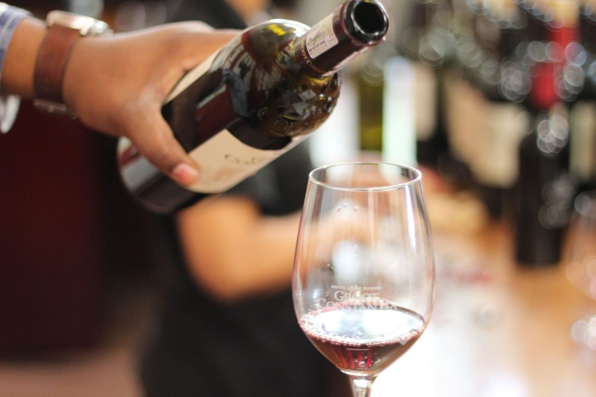 Main versant du vin dans un verre, table et bouteilles de vin en arrière-plan