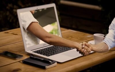 Laptop montrant un bras, main tendue, table en bois, smartphone, stylo, tasse de café