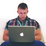 Homme assis sur un canapé, travaillant sur un MacBook ouvert devant lui