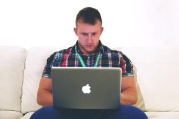 Homme assis sur un canapé, travaillant sur un MacBook ouvert devant lui