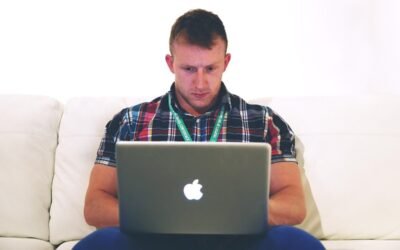 Homme assis sur un canapé, travaillant sur un MacBook ouvert devant lui