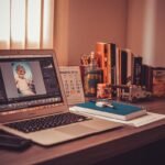 Un bureau avec ordinateur affichant une retouche photo, livres, cahier et stylo