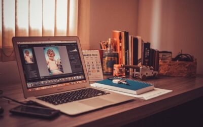 Un bureau avec ordinateur affichant une retouche photo, livres, cahier et stylo