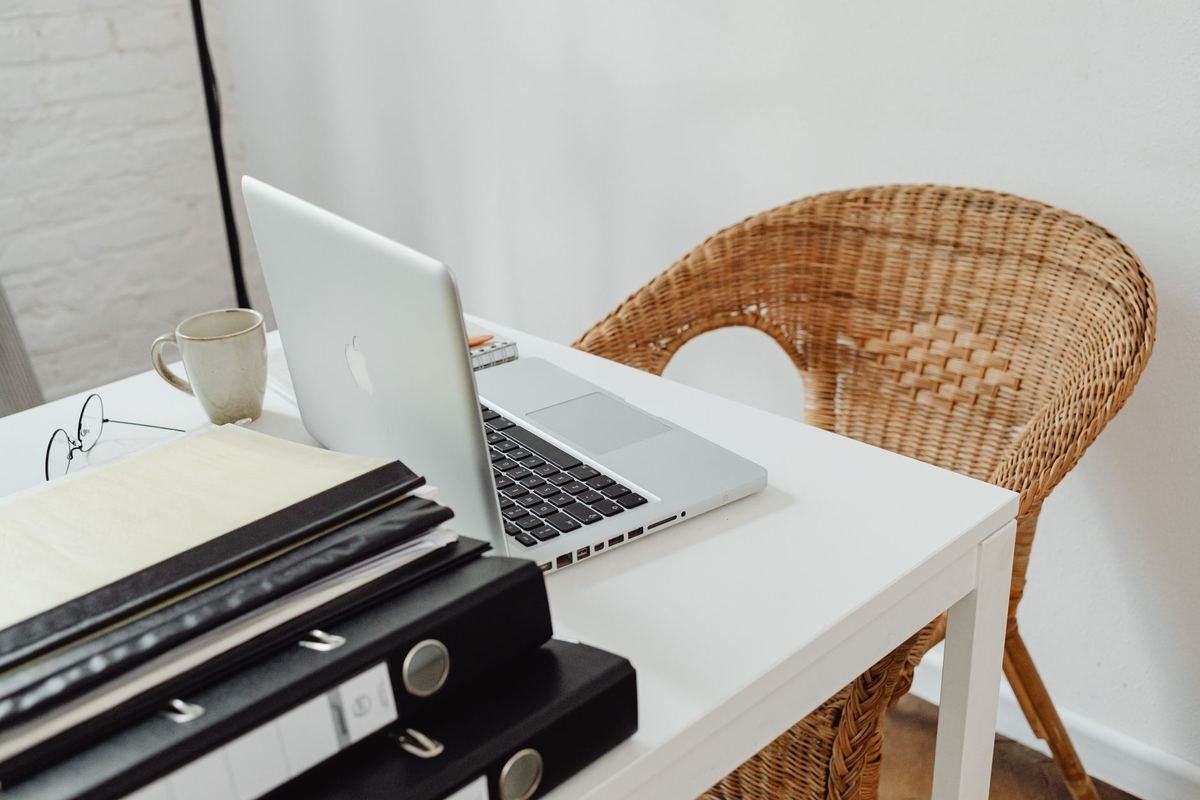 Un bureau avec ordinateur portable, tasse, dossiers et chaise en rotin Un bureau avec ordinateur portable, tasse, dossiers et chaise en rotin